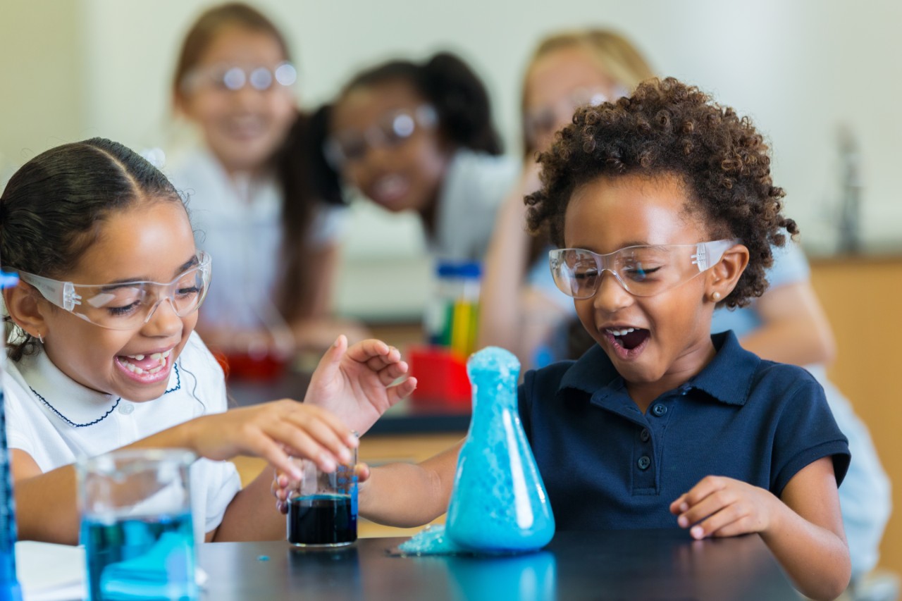 Diverse private school classmates are excited as foam overflows from beaker during chemistry experiment.