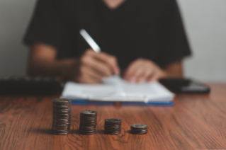person with a pen and paper and a stack of coins in front of them